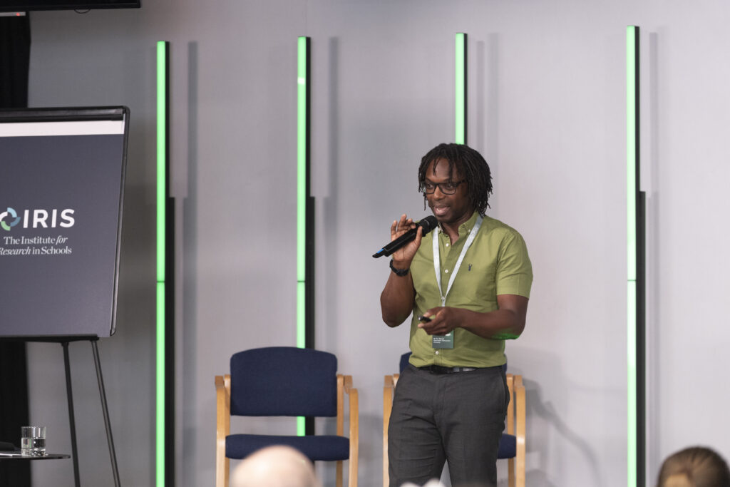 Manny Olaiya hold a microphone and presents on stage in Manchester