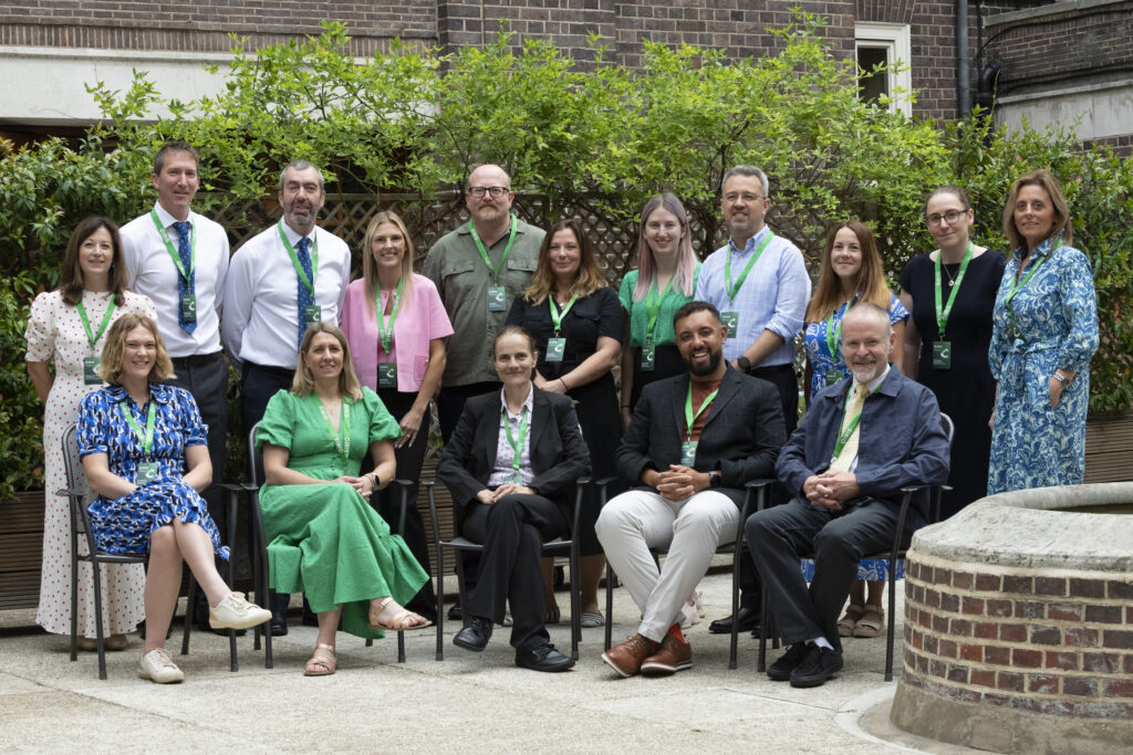 The IRIS team pose for a photo outside one of the 2025 conference venues. Director Jo Foster is sat in the middle. The whole team are smiling.