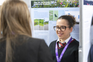 A female student stands next to her poster