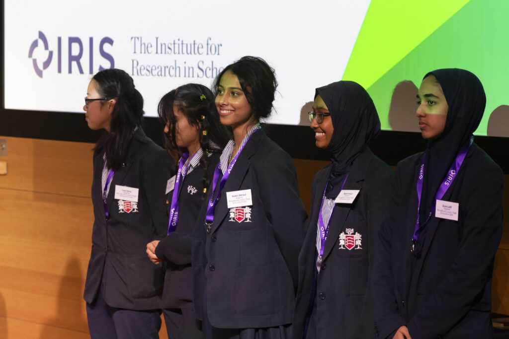 Five female students standing on stage in front of a presentation, smiling after winning an award.