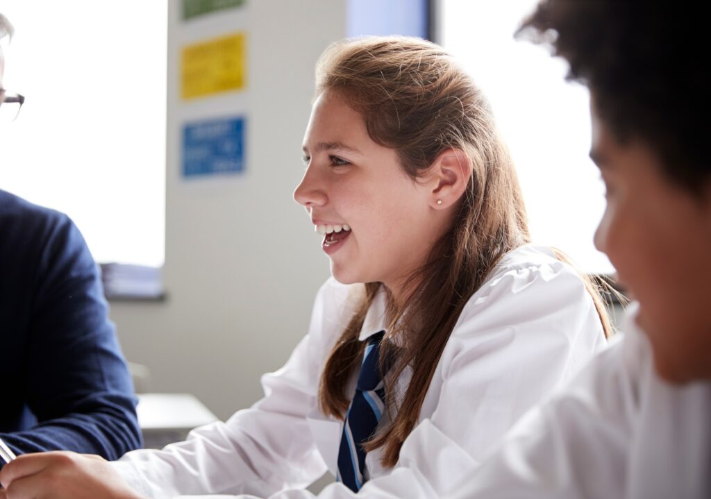 Female student smiling in UK classroom. To her right is a male student taking part in the conversation.
